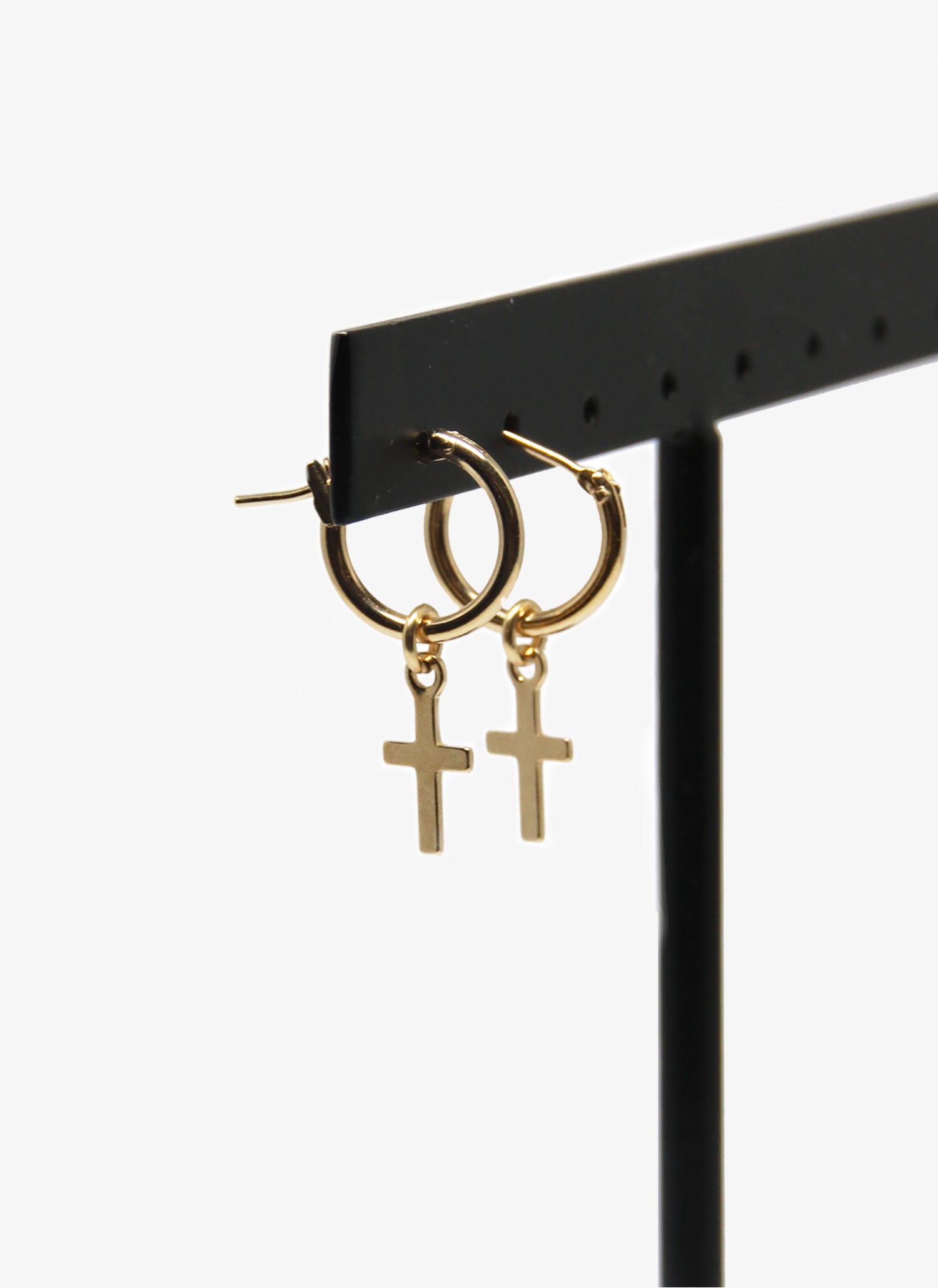 Gold hoop earrings with cross charms on a black stand against a white background